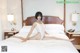 A woman in a white bodysuit sitting on a bed.