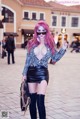 A woman with pink hair wearing a black leather skirt and thigh high boots.